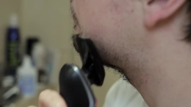 Młody człowiek z brodą golił ściernisko brzytwą elektryczną. — Wideo stockowe