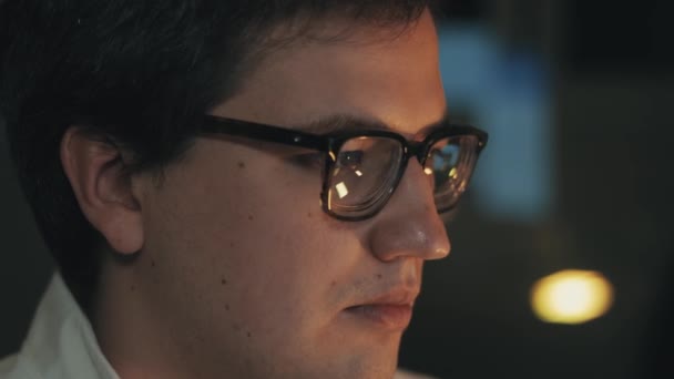 Hombre con gafas de vista tarde en la noche desplazándose delante de la computadora portátil — Vídeos de Stock