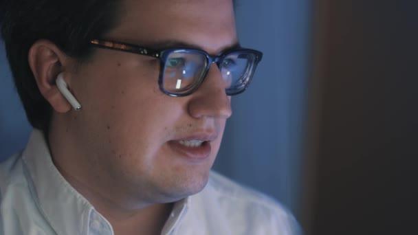 Молодой бизнесмен в наушниках разговаривает перед компьютером — стоковое видео