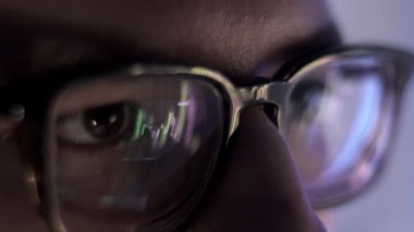 Gece geç saatte gözlüklü bir adam dizüstü bilgisayarın önünde kayıyor.