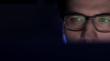 Gece geç saatte gözlüklü bir adam dizüstü bilgisayarın önünde kayıyor.