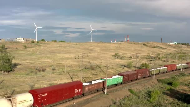 URAL REGION, RUSSIA - JULI 10, 2019: Goederentrein op de achtergrond van windmolens, drone schot onder grijze hemel — Stockvideo