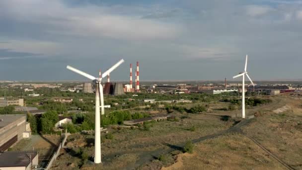 URAL REGION, RUSSIA - LIPIEC 10, 2019: Dwie turbiny wiatrowe pochylone w górę, na tle fabryk pod szarym niebem — Wideo stockowe