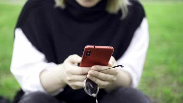 SMS dans un téléphone assis dans le parc sur une herbe floue et de l'eau