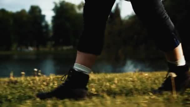Nogi w butach spacerujących na tle parku miejskiego, ujęcie profilowe — Wideo stockowe