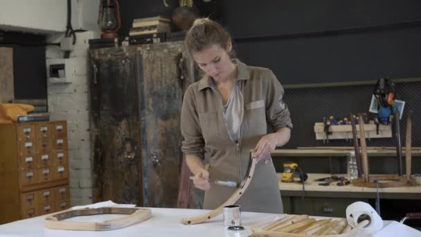 Nő fából készült szék lábát festi egy műhelyben, helyreállítási folyamat — Stock videók