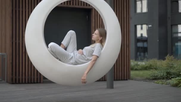 Wanita muda dalam ayunan futuristik putih di halaman luar — Stok Video