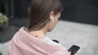 Genç bir kadın telefonu kaydırıyor, kulaklık takıyor, en iyi görüntü.