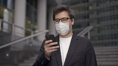 Takım elbiseli ve yüz maskeli bir adam kendini yeni ve korkunç virüslerden korumak için şehir merkezindeki finans merkezindeki akıllı telefonları kullanıyor.. 