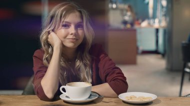 Kafede rüya gören ve toplantı bekleyen çekici, güler yüzlü bir kadın. Doğrudan kameraya bakıyor. İşaret fişeği