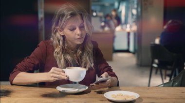 Kafede internete girip akıllı telefon kullanan ve arkadaşlarıyla buluşmayı bekleyen çekici bir kadın. İşaret fişeği