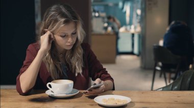 Kafedeki çekici kadın internette akıllı telefon kullanıyor ve arkadaşlarıyla buluşmayı bekliyor.. 