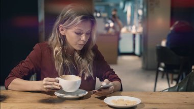Kafede internete girip akıllı telefon kullanan ve arkadaşlarıyla buluşmayı bekleyen çekici bir kadın. İşaret fişeği