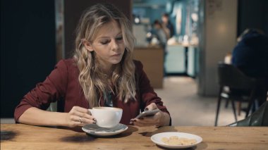 Kafede internete girip akıllı telefon kullanan ve arkadaşlarıyla buluşmayı bekleyen çekici bir kadın. İşaret fişeği