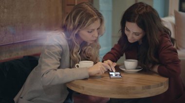Kafede sohbet eden ve bazı dedikoduları tartışan iki çekici kadın akıllı telefonda sosyal ağları kullanıyor. Arkadaşlık ve feminizm kavramı. 