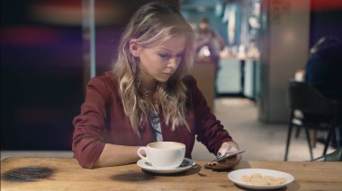Kafede internete girip akıllı telefon kullanan ve arkadaşlarıyla buluşmayı bekleyen çekici bir kadın. İşaret fişeği