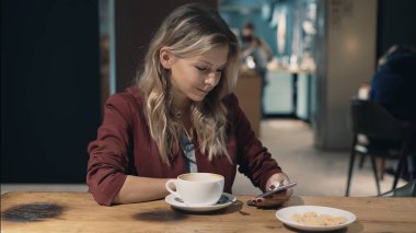Kafede internete girip akıllı telefon kullanan ve arkadaşlarıyla buluşmayı bekleyen çekici bir kadın. İşaret fişeği