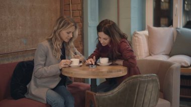 Kafede sohbet eden ve bazı dedikoduları tartışan iki çekici kadın akıllı telefonda sosyal ağları kullanıyor. Arkadaşlık ve feminizm kavramı. 
