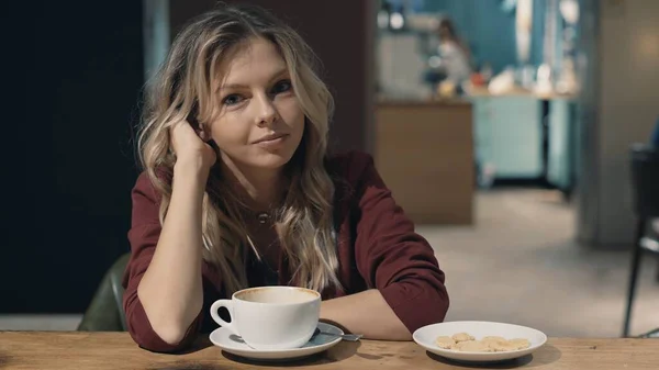 Attraente donna sorridente in caffè sognando e in attesa di un incontro. guardando direttamente alla macchina fotografica — Foto Stock