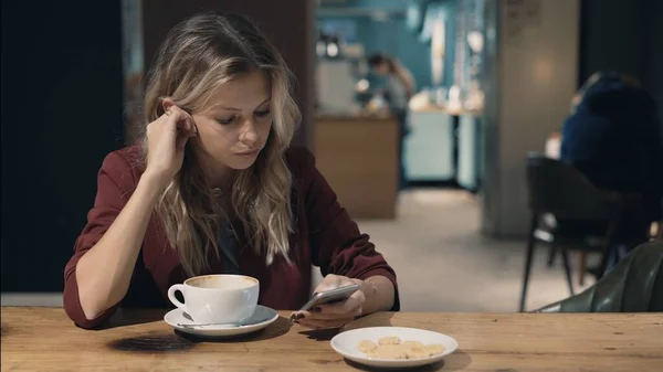 Mujer atractiva en la cafetería navegando por Internet utilizando el teléfono inteligente y esperando una reunión con un amigo. — Foto de Stock