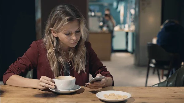 Mujer atractiva en la cafetería navegando por Internet utilizando el teléfono inteligente y esperando una reunión con un amigo. — Foto de Stock