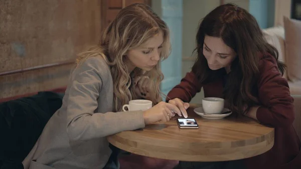 Kafede sohbet eden ve bazı dedikoduları tartışan iki çekici kadın akıllı telefonda sosyal ağları kullanıyor. Arkadaşlık ve feminizm kavramı. — Stok fotoğraf