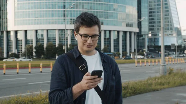 İş merkezi binasının arka planındaki genç adam telefonla mesajlaşıyor.