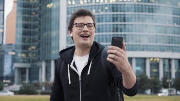 Uomo che fa una videochiamata, usa auricolari, cammina sullo sfondo del business center — Video Stock