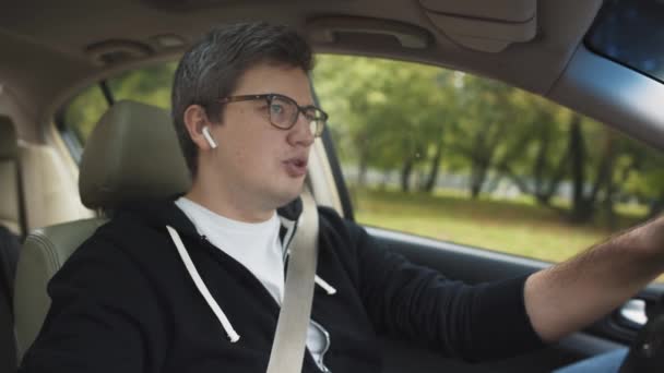 Man in eyeglasses using earpods in a car, dressed in casual clothes — Stock Video