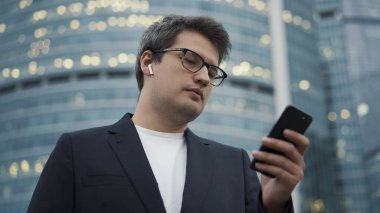 Kulaklıklı bir adam iş merkezinin arka planında telefonuyla ayakta duruyor.