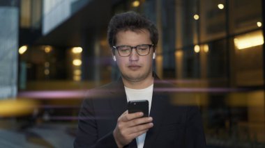 Akşam telefonu kaydıran adam cam pencerelerin arkasında duruyor.