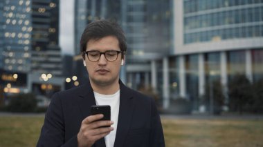 Kulaklıklı bir adam iş merkezinin arka planında telefonuyla ayakta duruyor.