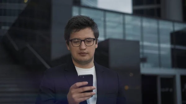 Чоловік у костюмі стоїть з телефоном на фоні скляних будівель — стокове фото