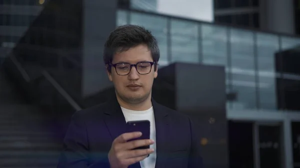 Чоловік у костюмі стоїть з телефоном на фоні скляних будівель — стокове фото