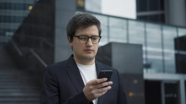 Homem de terno de pé com um telefone no fundo de edifícios de vidro — Fotografia de Stock