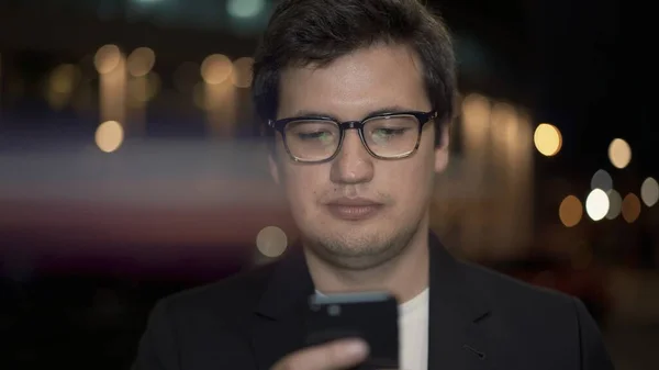 Бізнесмен в окулярах прокручує телефон на фоні, блимає лінза — стокове фото