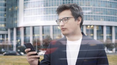 İş merkezinin arka planında telefonu olan takım elbiseli bir adam duruyor.