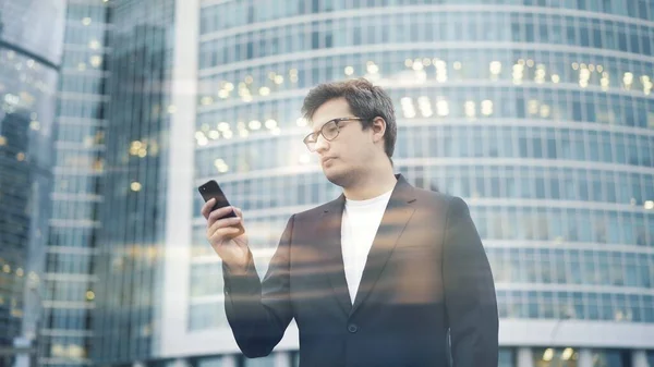 Чоловік стоїть з телефоном на фоні ділового центру — стокове фото