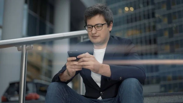 Empresário sentado em escadas, lente de sinalização, com telefone no fundo de edifícios de vidro — Fotografia de Stock