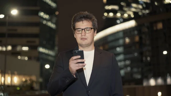 Бізнесмен в окулярах прокручує телефон в оточенні будівель — стокове фото