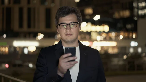 Empresario con el teléfono en el fondo de las luces nocturnas de la ciudad —  Fotos de Stock