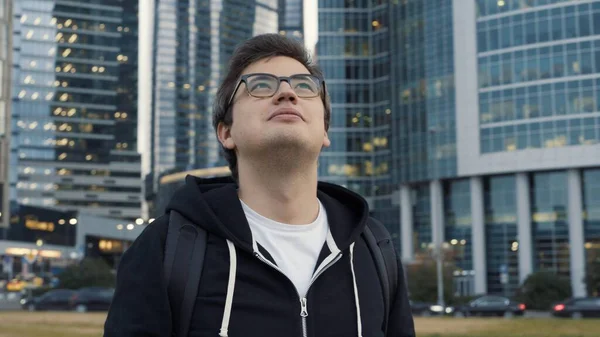 Homem de óculos sorrindo tiro do meio olhando para edifícios do centro de negócios — Fotografia de Stock