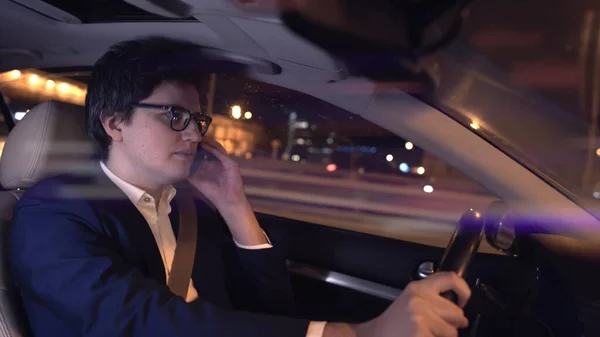 Man driver on the phone in black suit and eyeglasses at night, lens flare