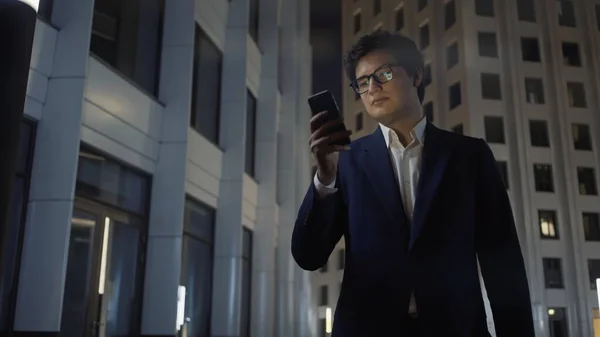 Man in black suit with phone surrounded by buildings, work at night