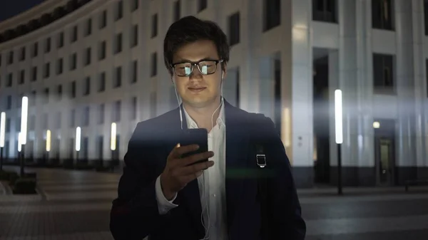 Homem sorrindo olhando para o telefone, sinalizador de lente de tiro da cidade noite — Fotografia de Stock
