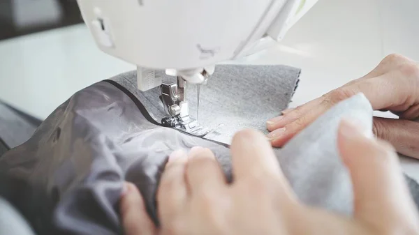 Costura de tela gris en una máquina de coser blanca, manos femeninas — Foto de Stock