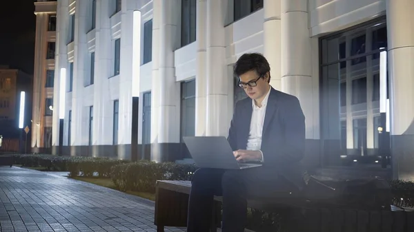 Homem com laptop no colo sentado no banco fora da universidade — Fotografia de Stock