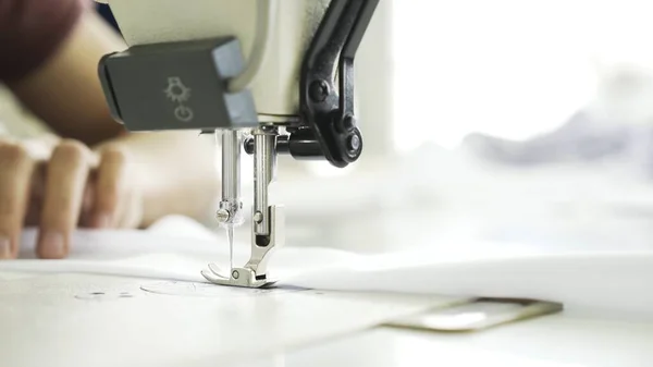 Sewing on machine, close up of hands and white cloth