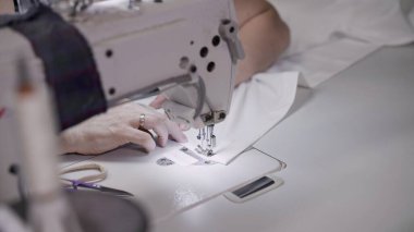 Beyaz bir dikiş makinesine beyaz bez diken kadın eller.