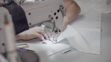 Beyaz bir dikiş makinesine beyaz bez diken kadın eller.